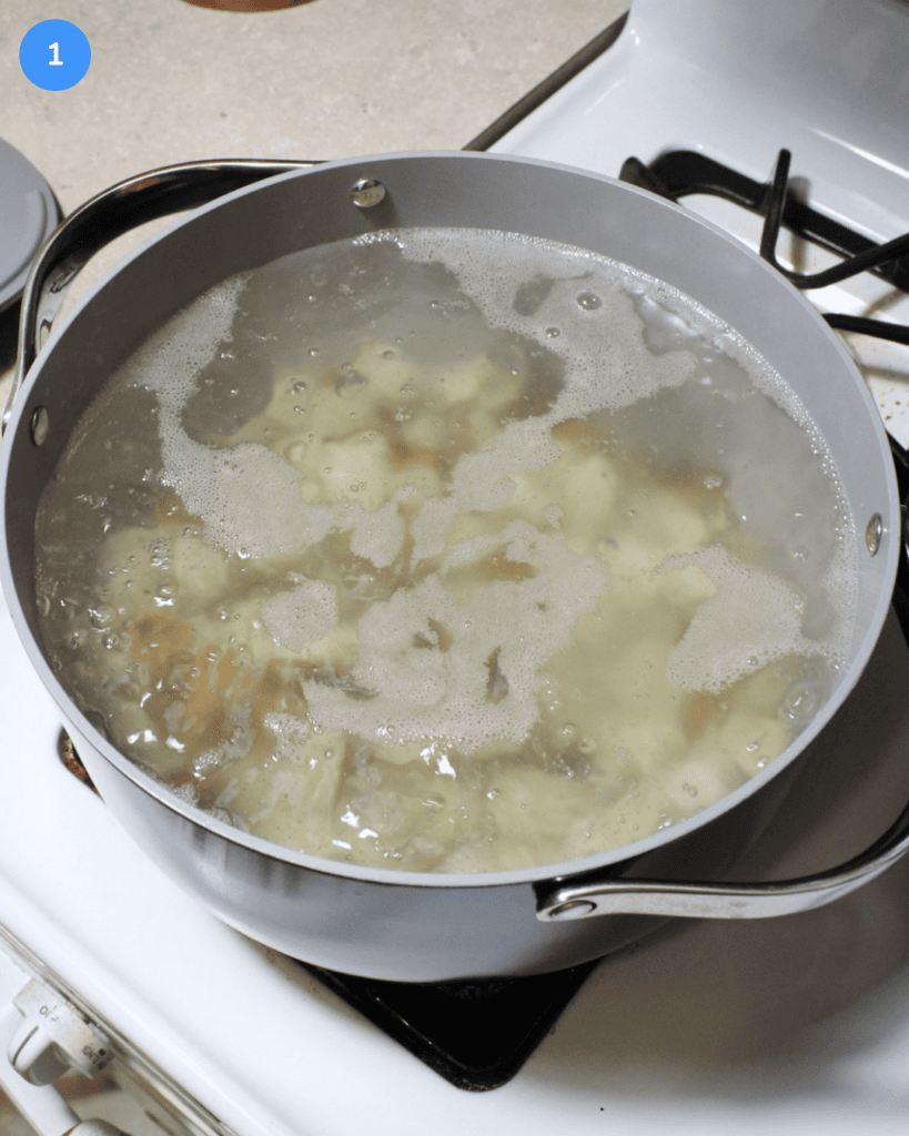A ceramic pot of boiling water with cubed russet potatoes cooking in it.