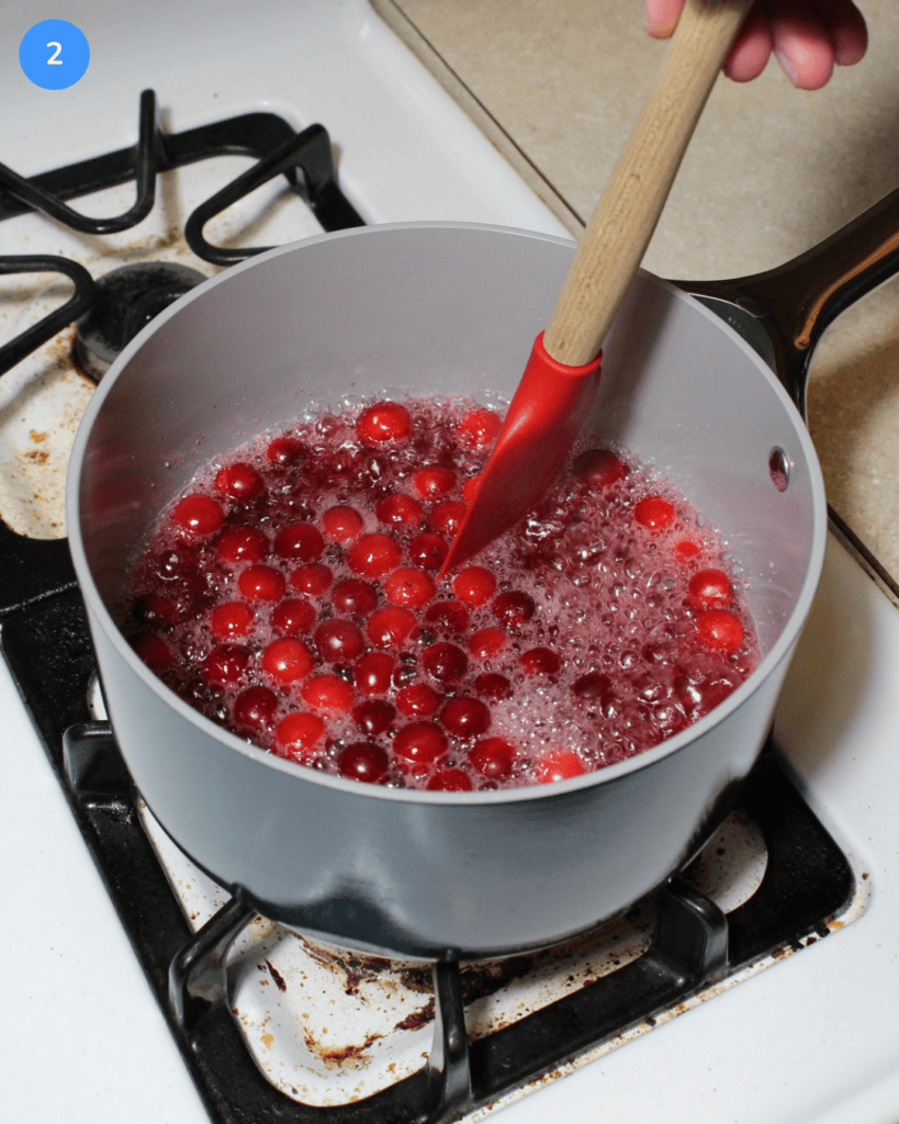 Cranberry simple syrup simmering on the stove being stirred with a rubber spatula.