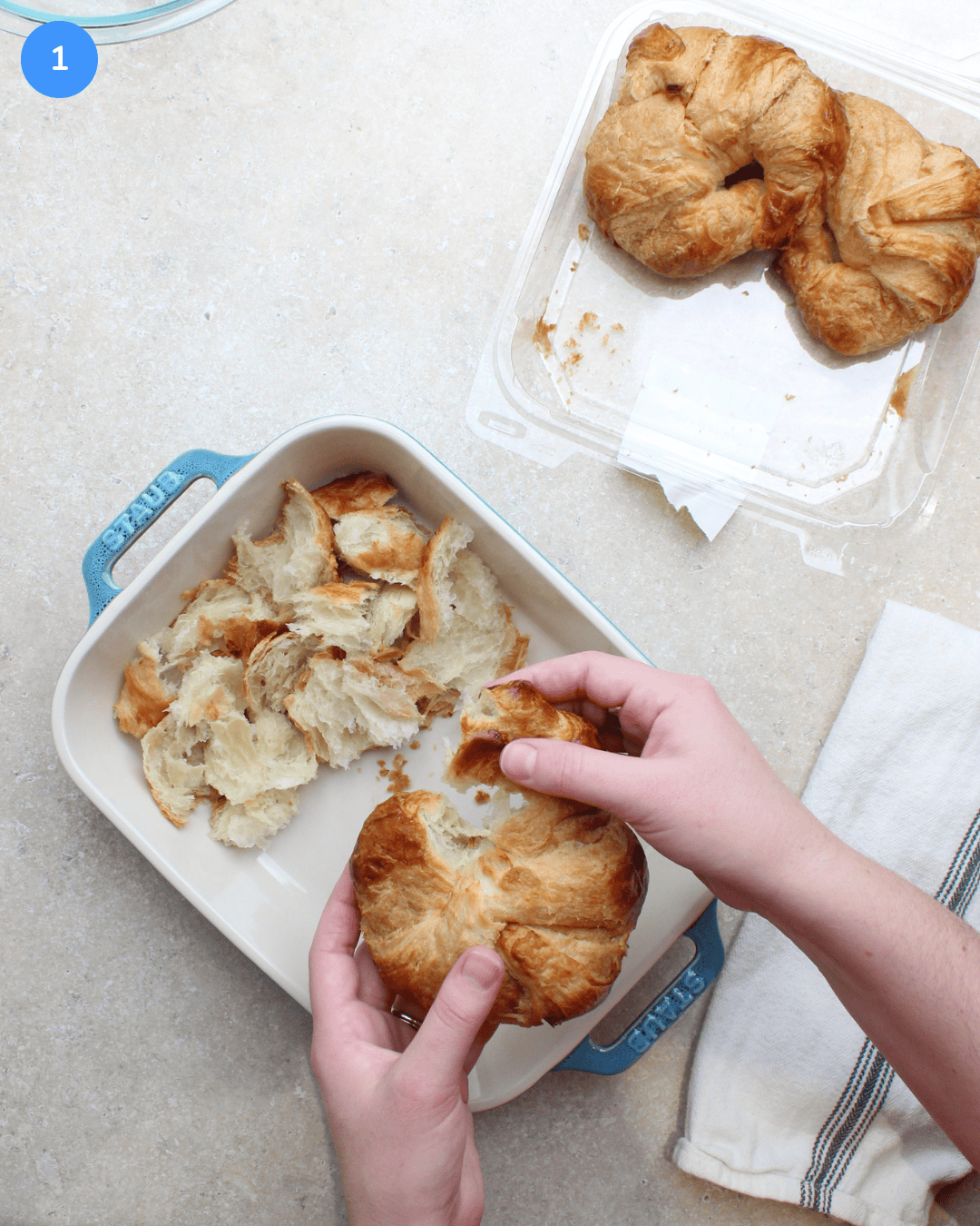 Ripping up store bought croissants into small pieces and putting them in a ceramic casserole dish.