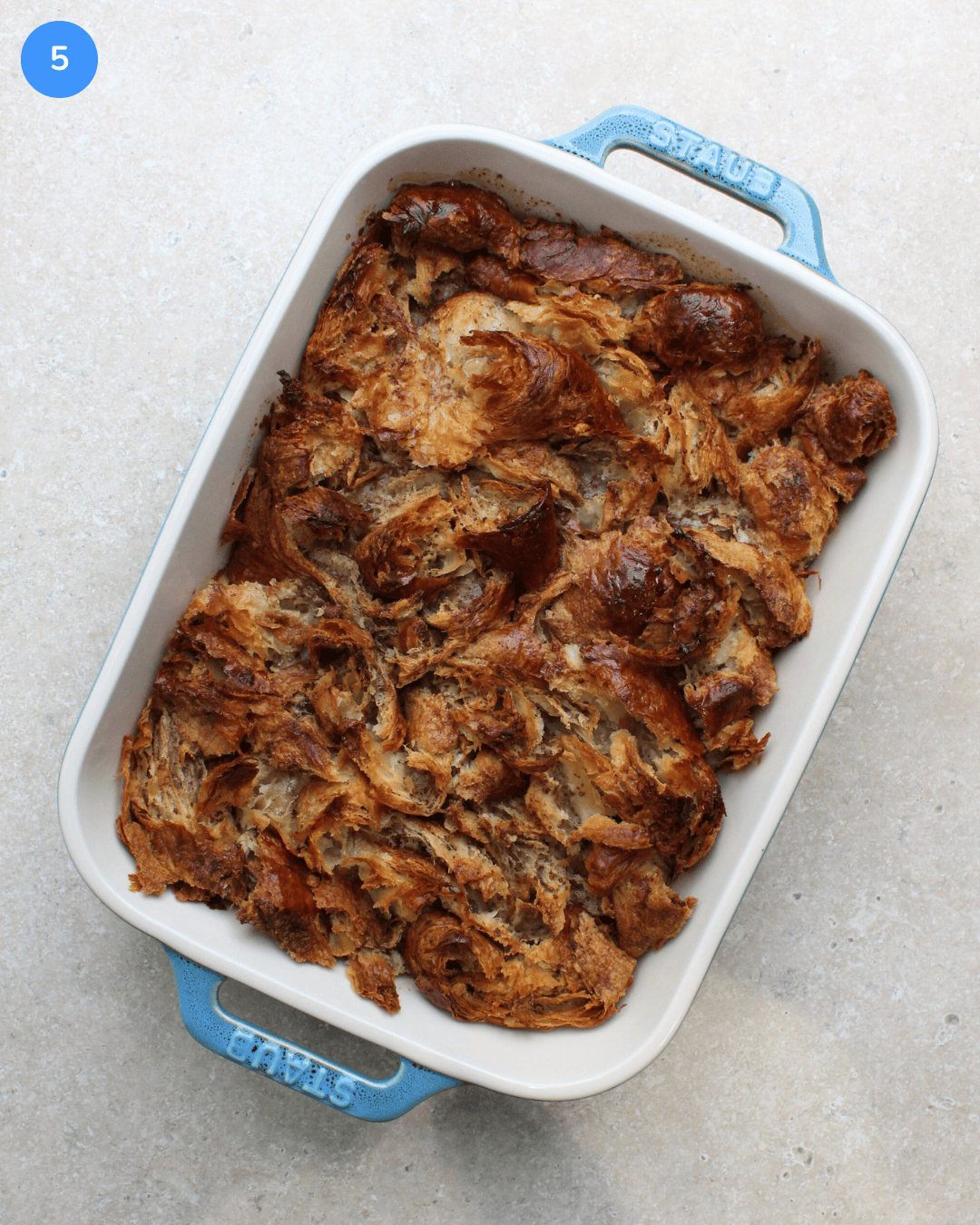 A blue ceramic casserole dish of freshly baked croissant french toast.