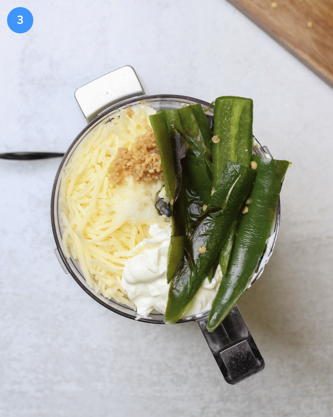 A food processor with cream cheese, greek yogurt, cheddar cheese, garlic, salt, and roasted jalapenos in it.