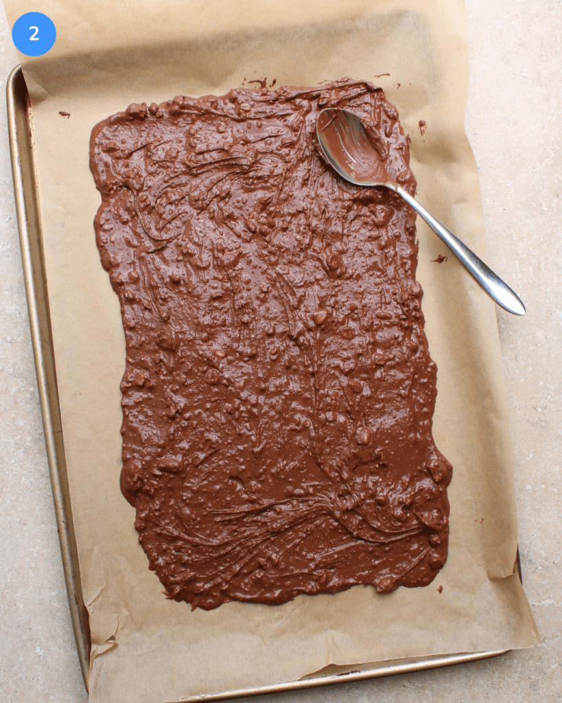 Melted milk chocolate and candy canes spread on a parchment lined baking sheet.