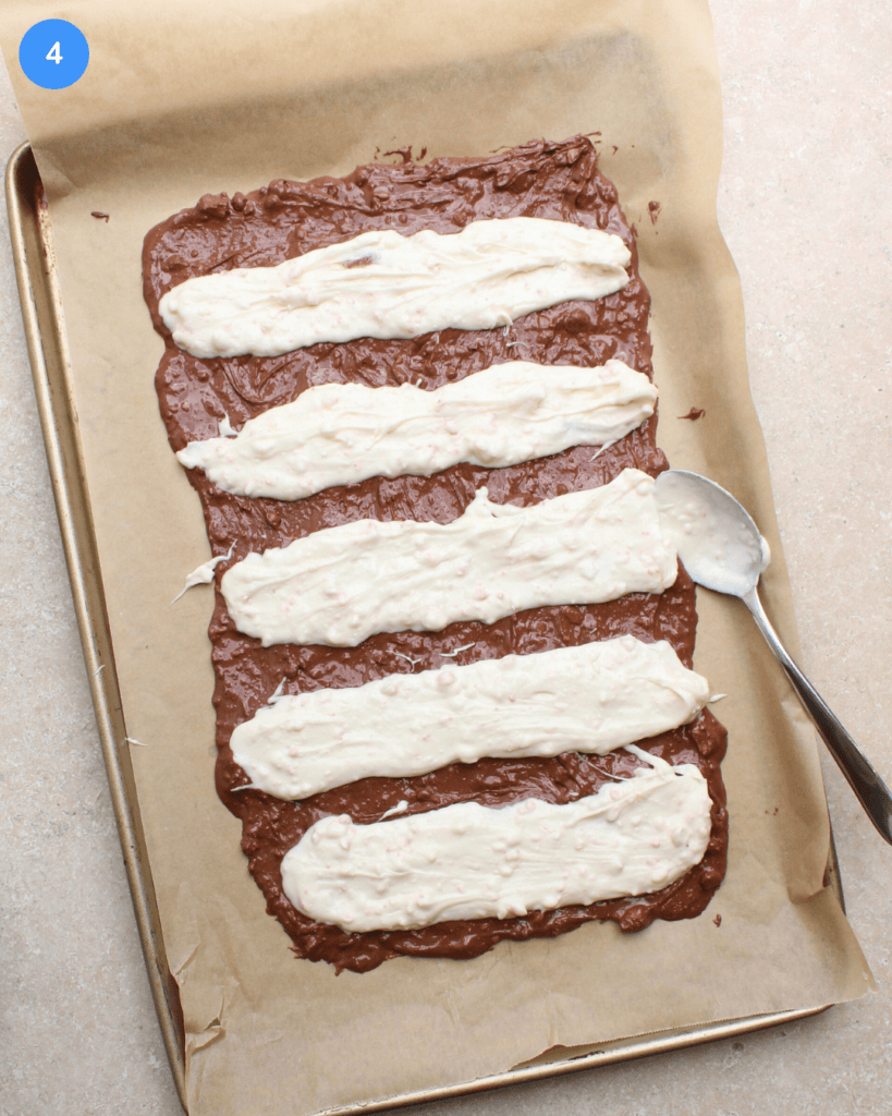 A layer of melted milk chocolate on a parchment lined baking sheet, topped with thick lines of melted white chocolate.