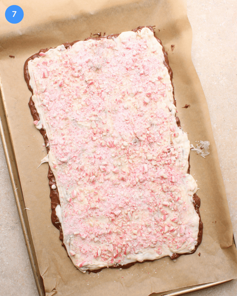 Milk and white chocolate peppermint bark topped with crushed candy canes on a parchment lined baking sheet.