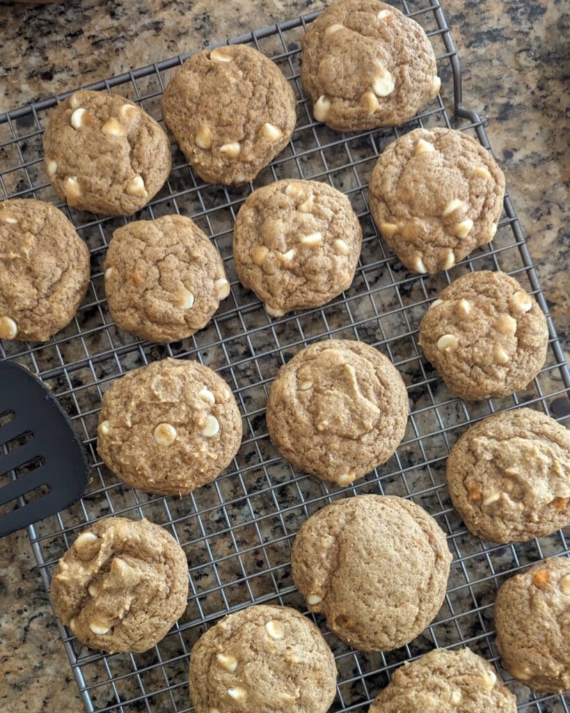A batch of freshly baked sweet potato white chocolate chip cookies on a wire cooling rack.