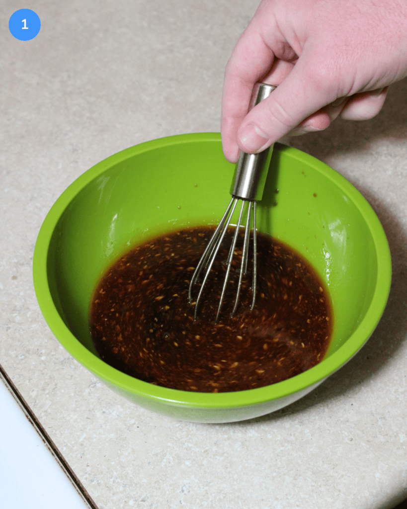 A soy sauce, brown sugar, vinegar, and chili oil mixture being whisked in a small green bowl.