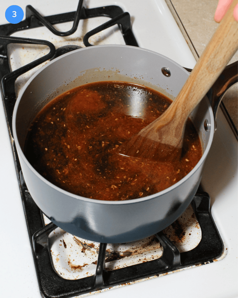 A blue ceramic saucepan on the stove with Szechuan soup being stirred.