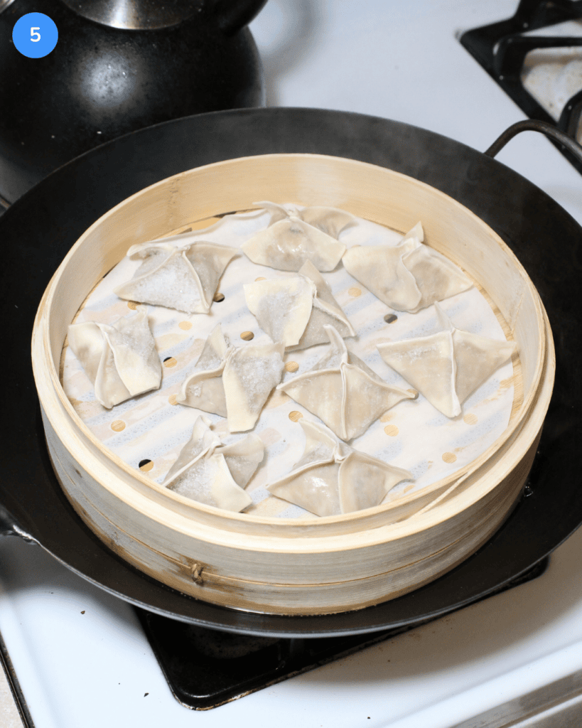 A bamboo steamer basked in a large wok with frozen pork dumplings in it, ready to be cooked.