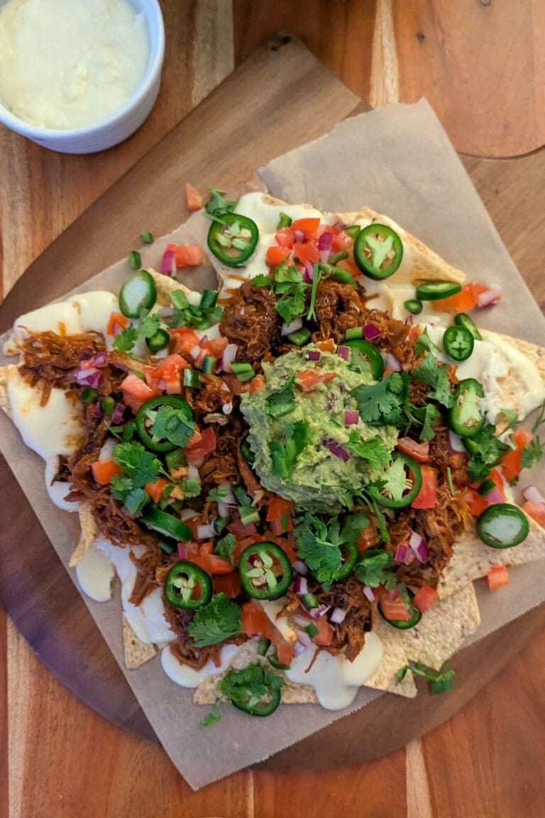 A platter of barbecue pulled pork nachos with cheese sauce, pico de gallo, jalapeno wheels, and fresh guacamole.