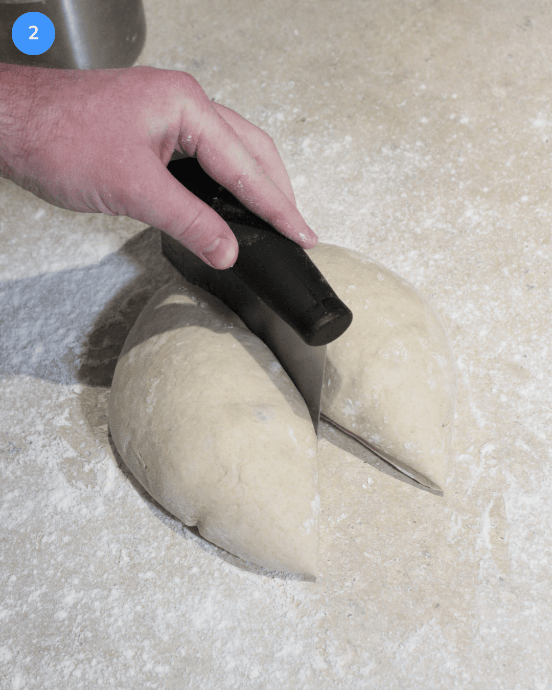 A ball of pizza dough being split in half with a bench knife on a floured work surface.