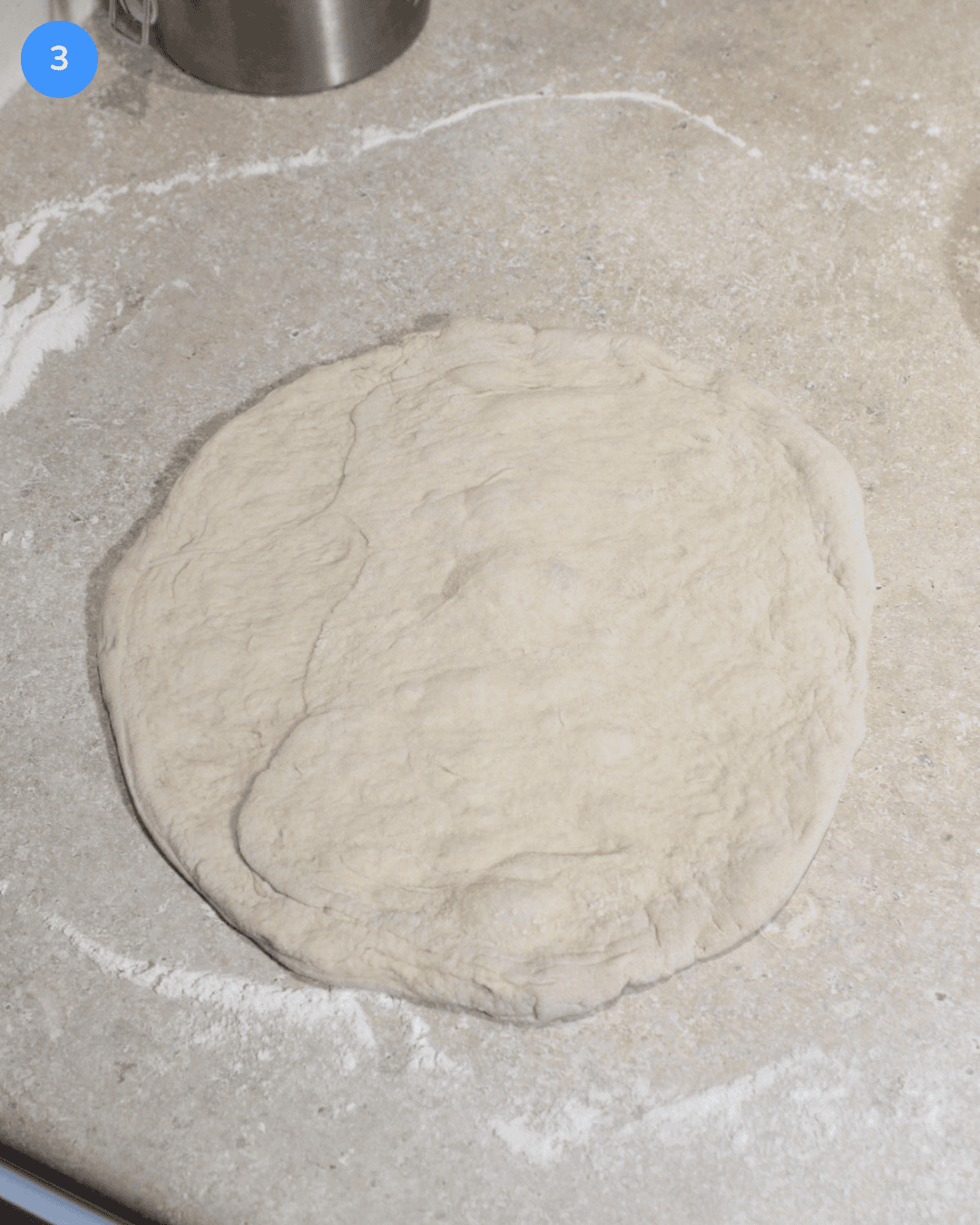 Unbaked pizza dough stretched into a circle on a floured counter.