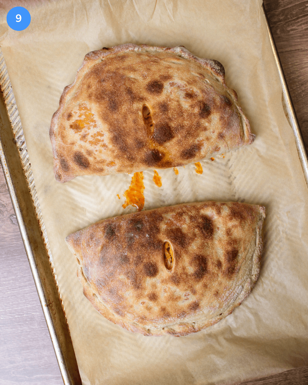 Two freshly baked buffalo chicken calzones on a parchment-lined baking sheet.