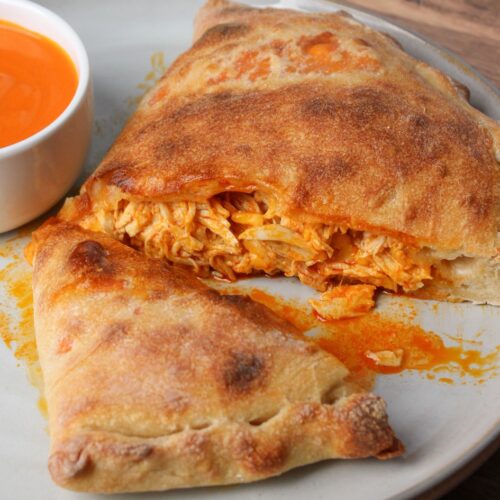 A cheesy, saucy buffalo chicken calzone cut in half on an off white ceramic plate.