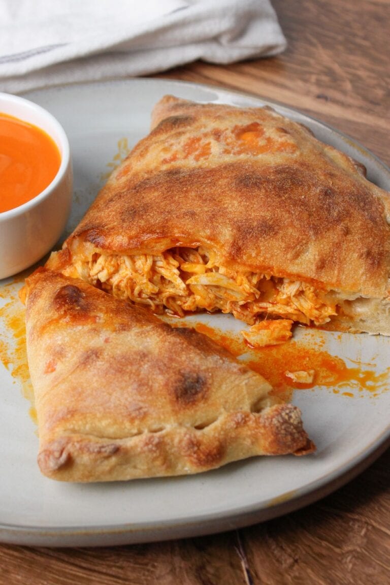 A cheesy, saucy buffalo chicken calzone cut in half on an off white ceramic plate.