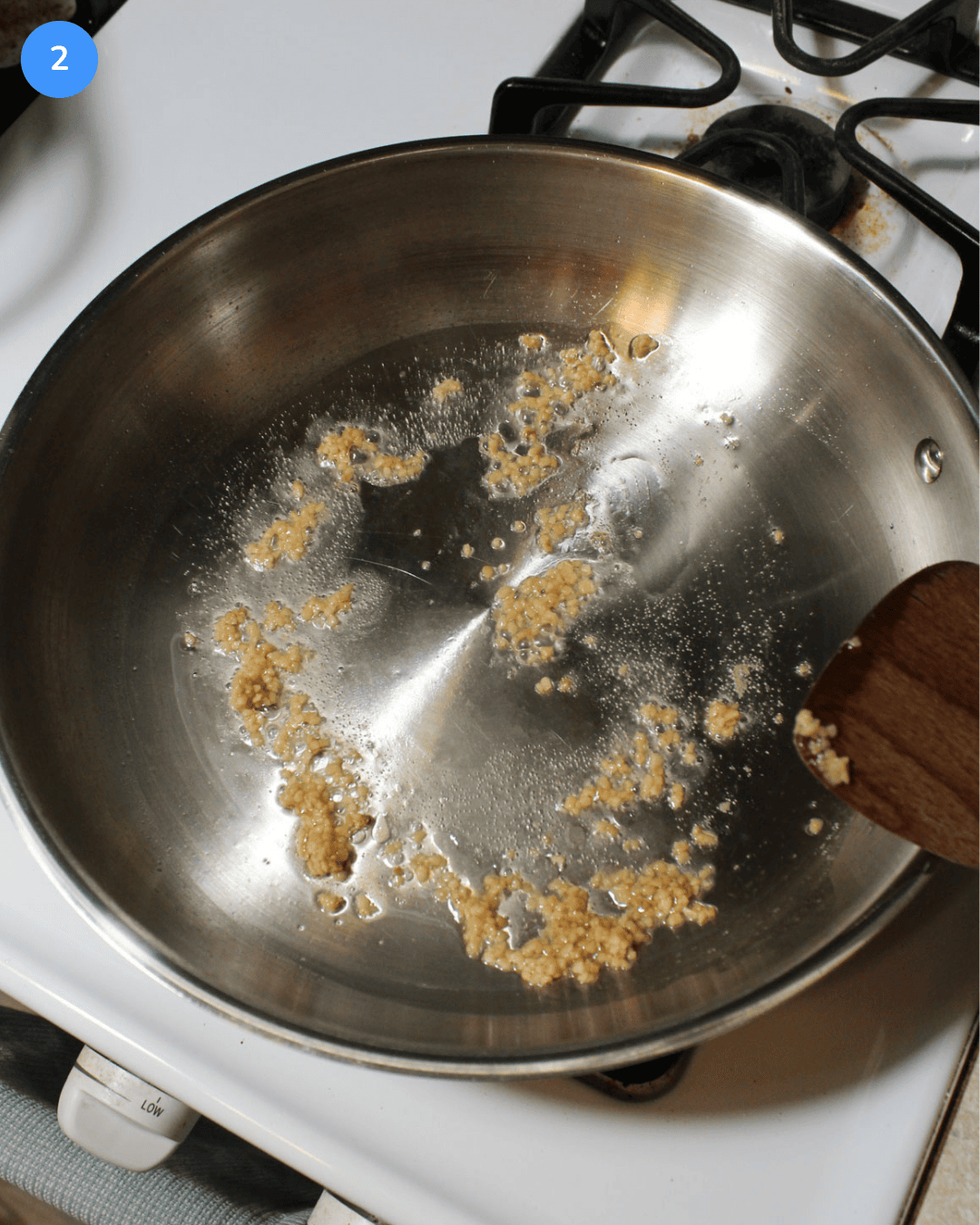 Minced garlic cooking in oil in a stainless steel frying pan.