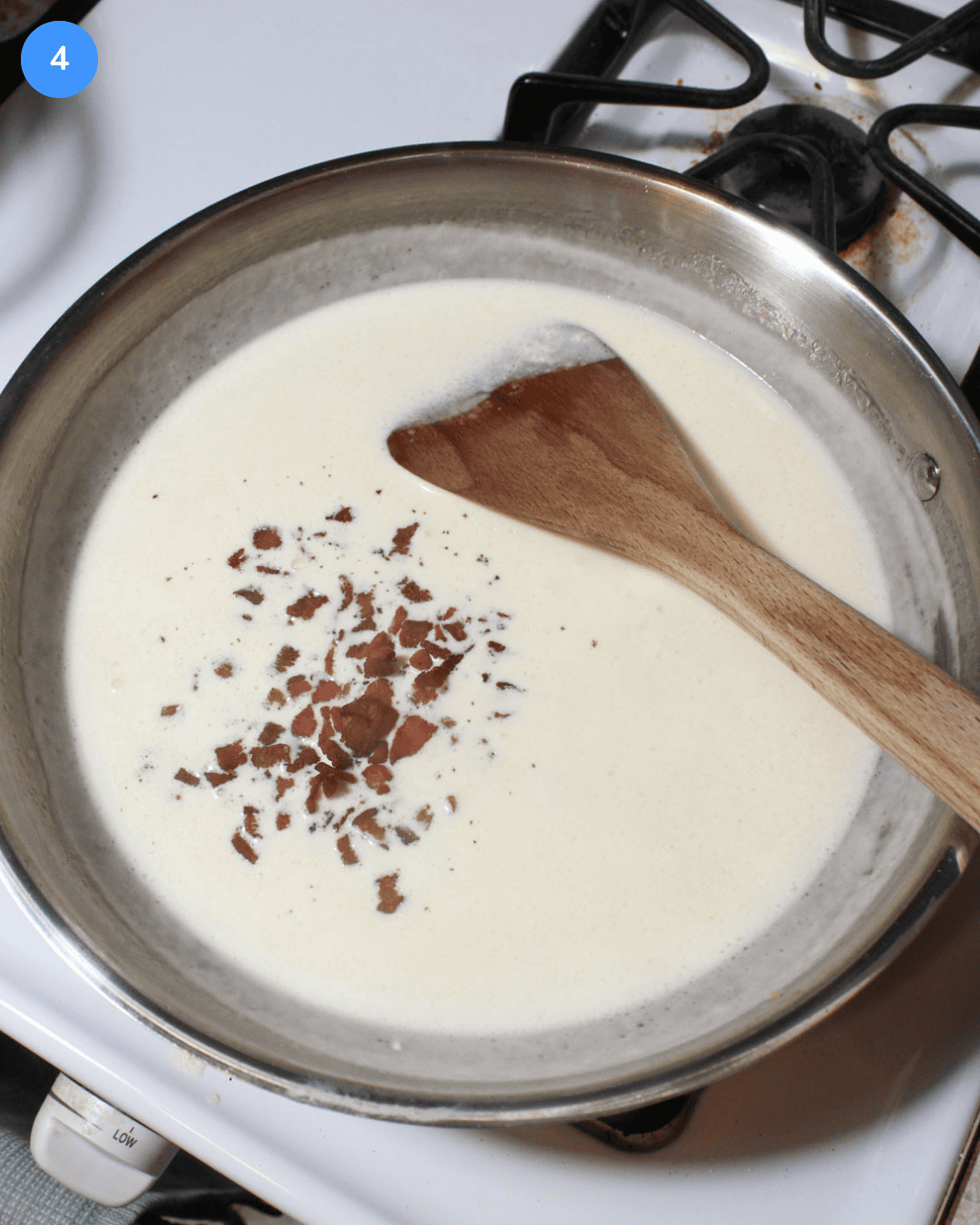 A cream sauce with bacon bits in a stainless steel frying pan.