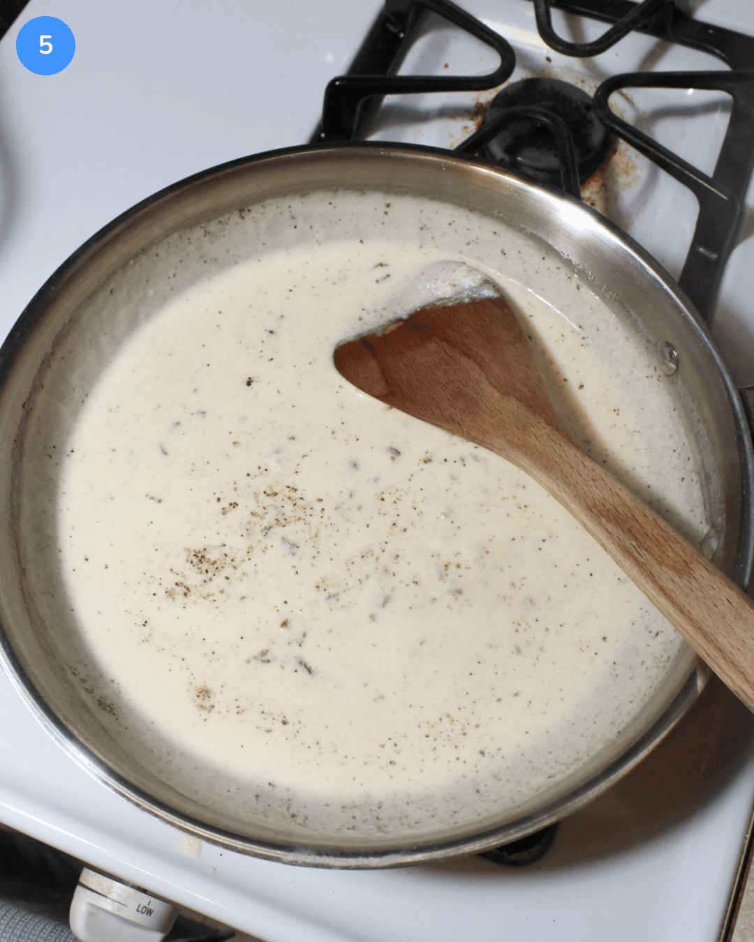 A cream sauce in a stainless steel frying pan seasoned with salt and black pepper.