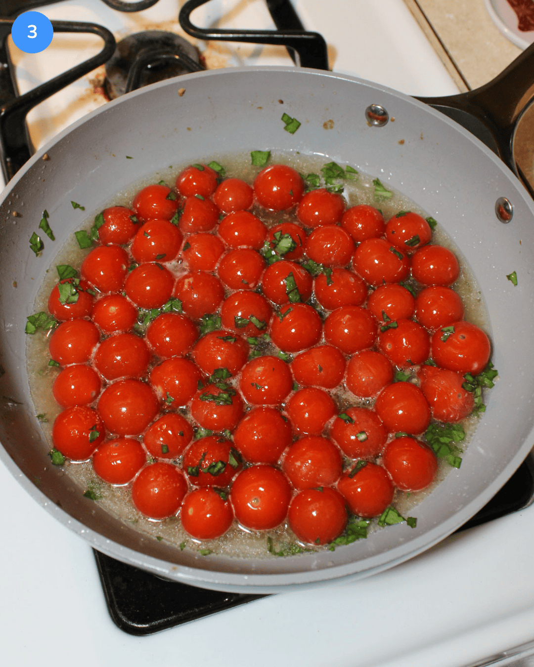Cherry tomatoes cooking in white wine with garlic and fresh basil in a ceramic frying pan on the stove.