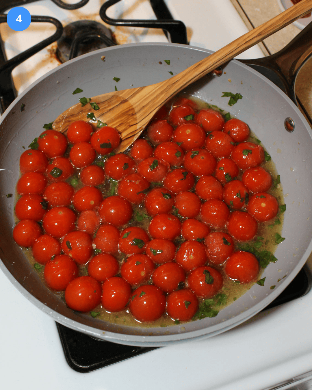 A ceramic non stick frying pan with cherry tomatoes and fresh basil cooking in a white wine, balsamic, and olive oil sauce with a wooden spoon.