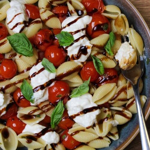 Burrata pasta with cherry tomatoes, fresh basil, and balsamic glaze in a blue stone bowl.