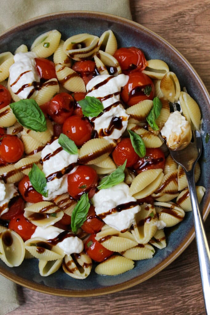 Burrata pasta with cherry tomatoes, fresh basil, and balsamic glaze in a blue stone bowl.