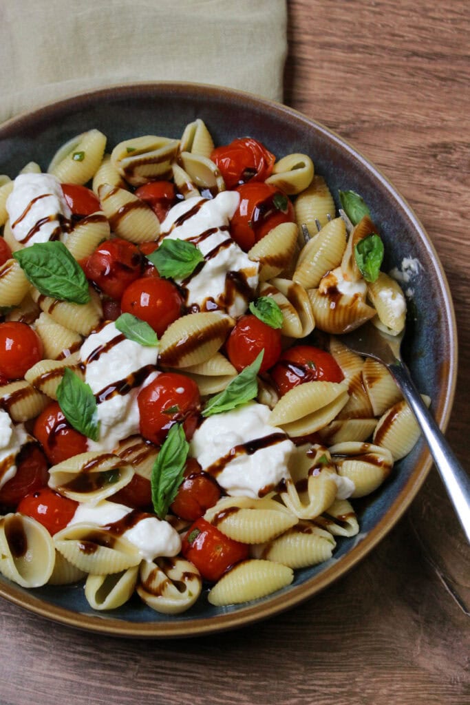 A blue stone bowl of burrata pasta with cherry tomatoes, fresh basil, and balsamic glaze.