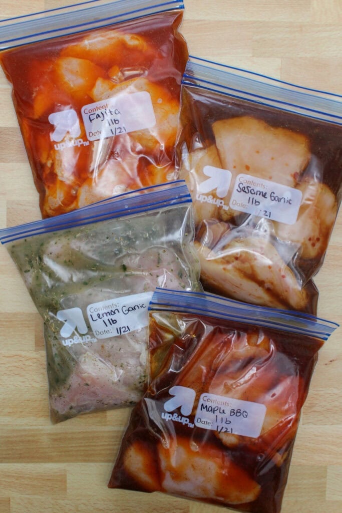 4 zip top bags of raw chicken in different marinades: fajita, sesame garlic, lemon garlic herb, and maple barbecue.