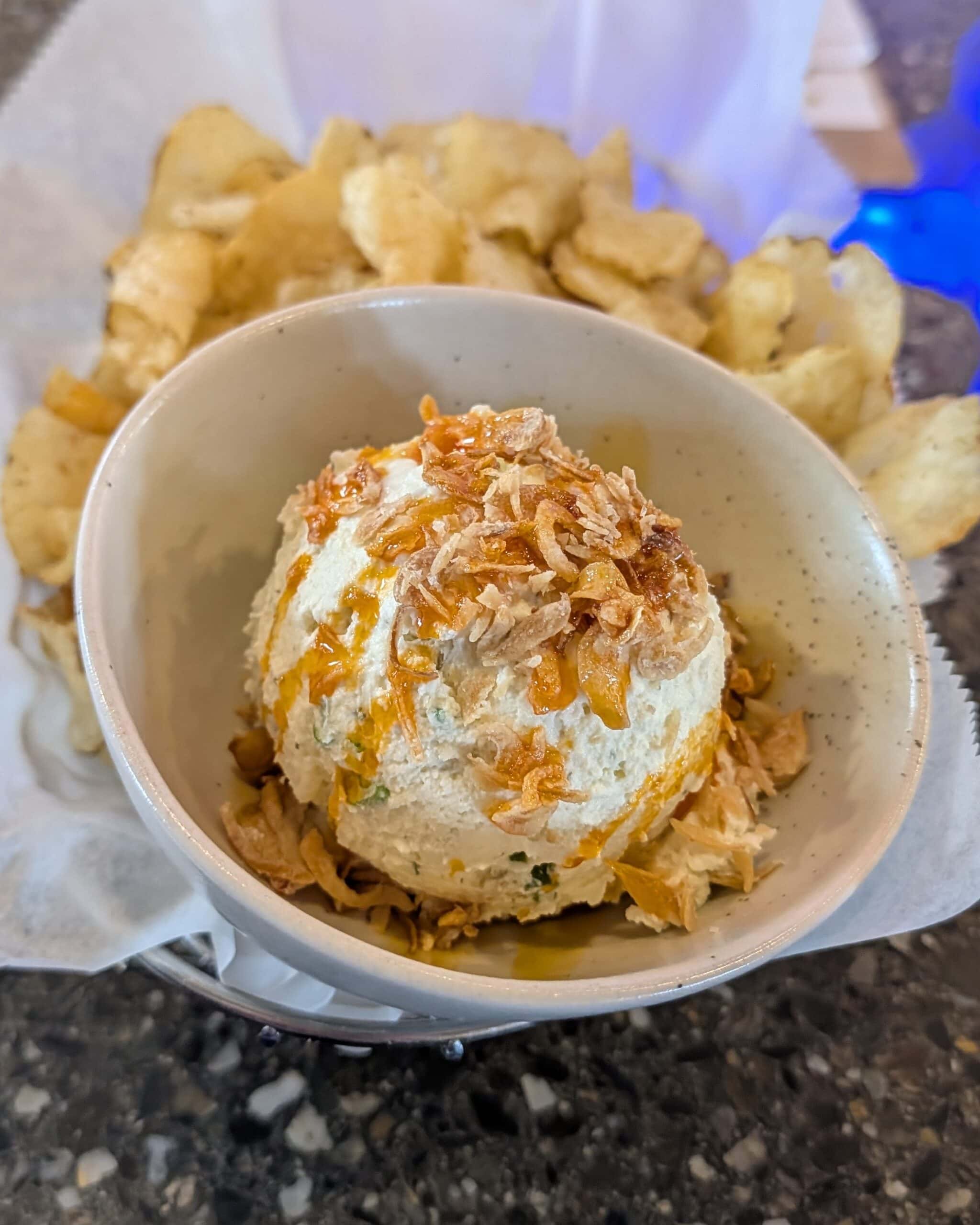 A ceramic bowl of onion dip topped with fried shallots, served with potato chips.