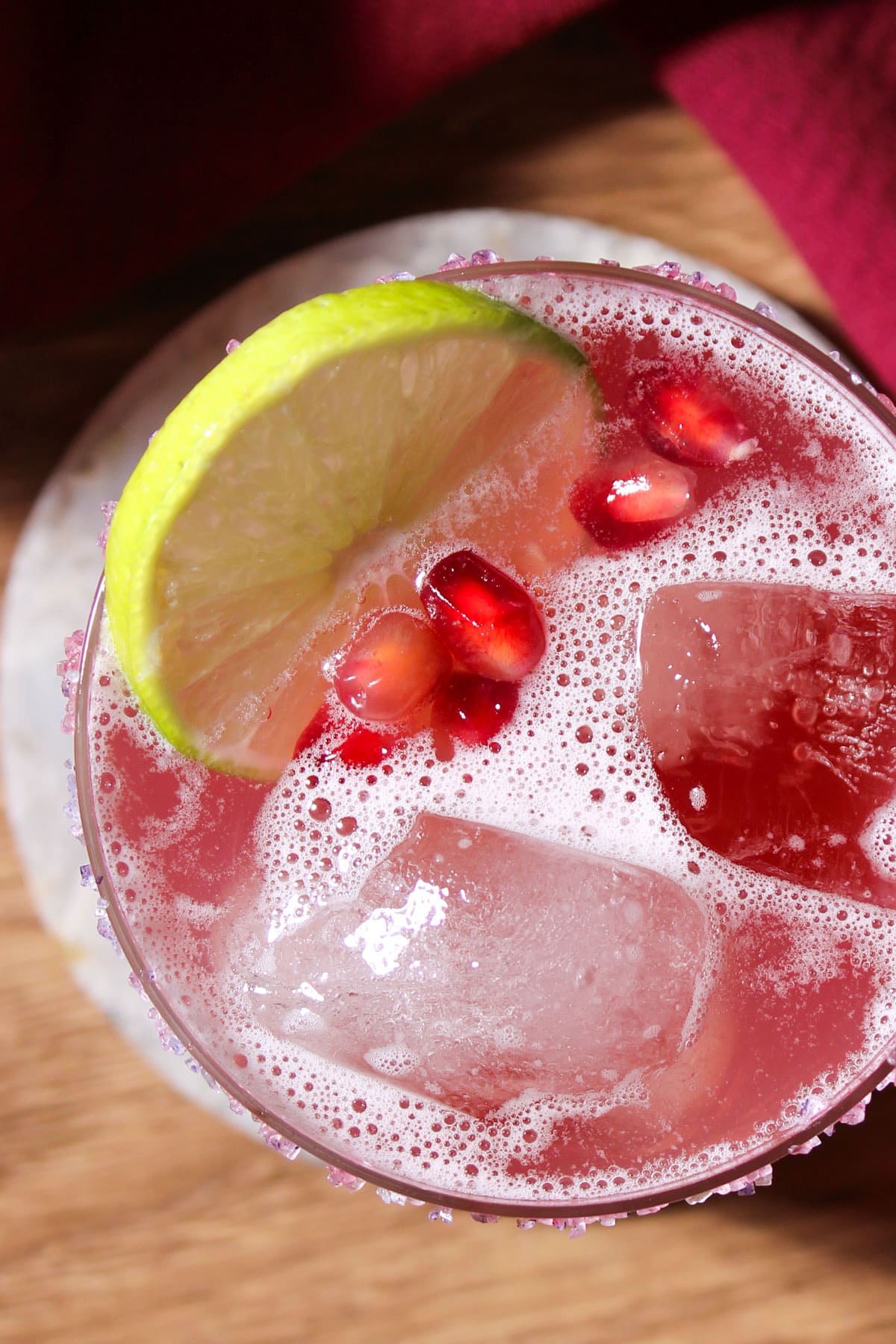 Garnishes on top of a pomegranate margarita on the rocks, including a lime wheel and fresh pomegranate arils.