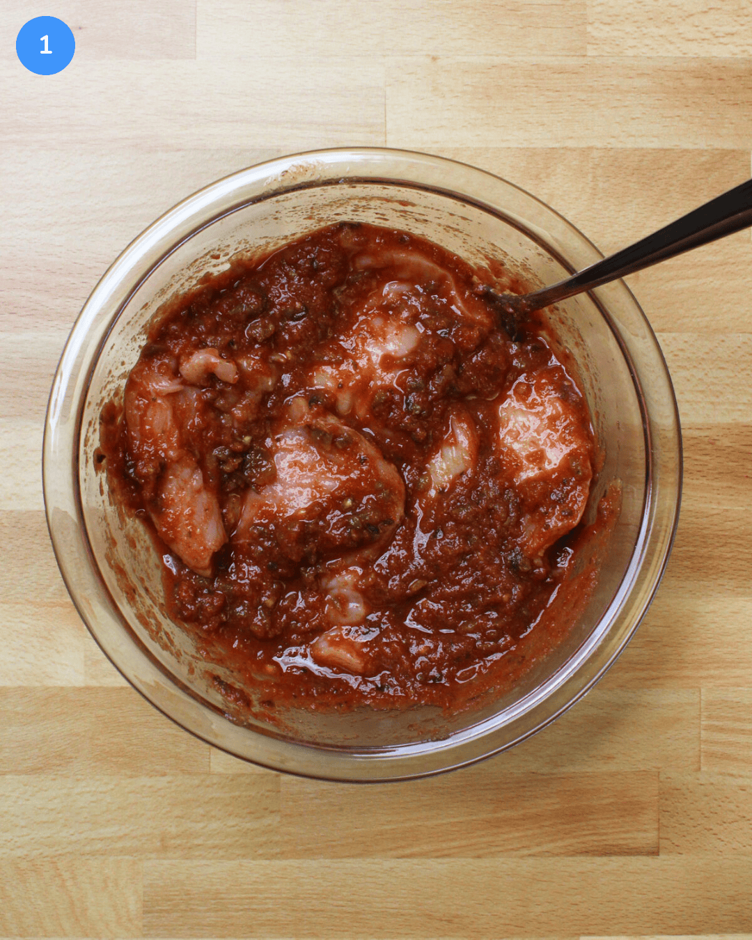 A glass bowl of chicken breast marinating in salsa, lime juice, and spices.