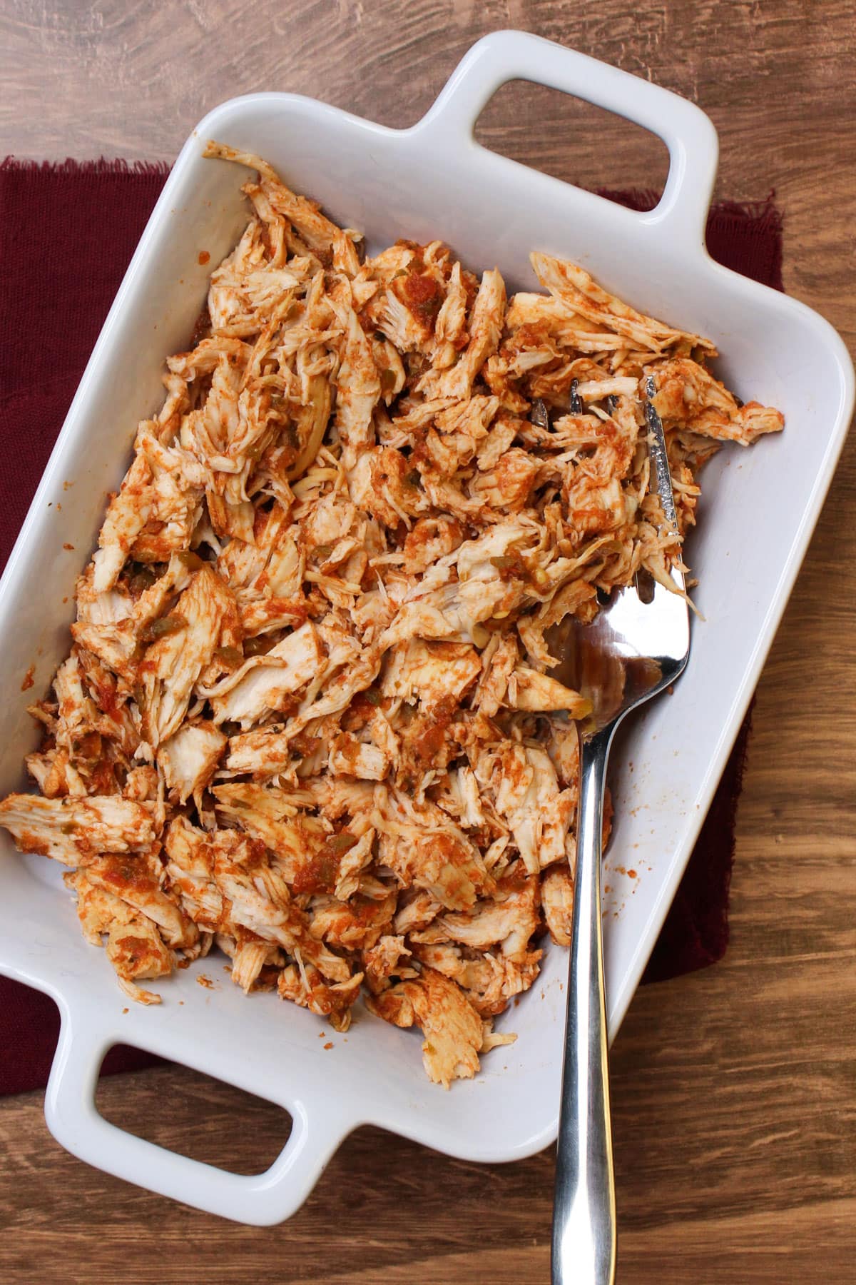 A serving dish of freshly shredded salsa marinated chicken with a large fork.
