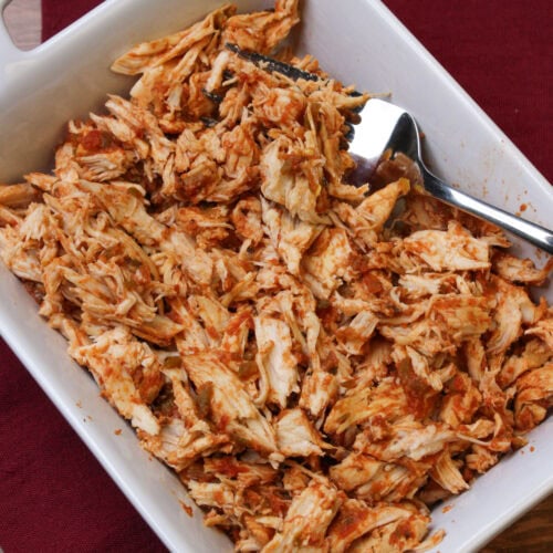 Shredded salsa marinated chicken in a white serving dish with a large fork for serving.