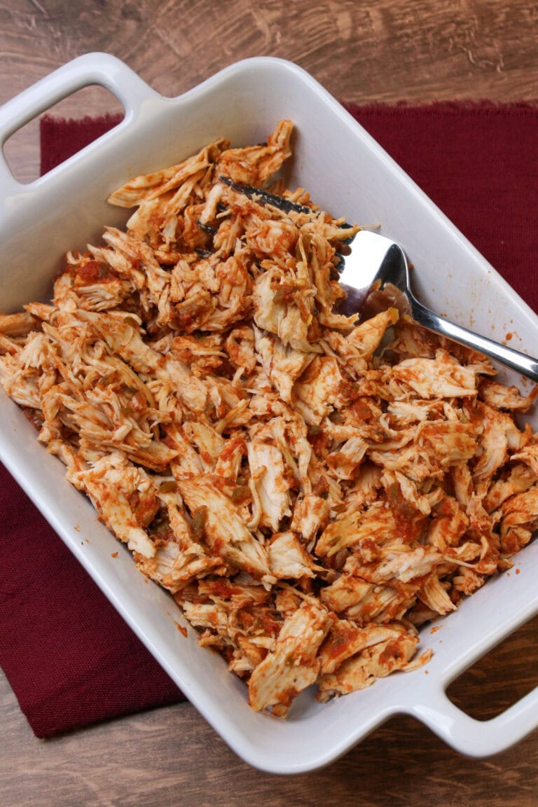 Shredded salsa marinated chicken in a white serving dish with a large fork for serving.