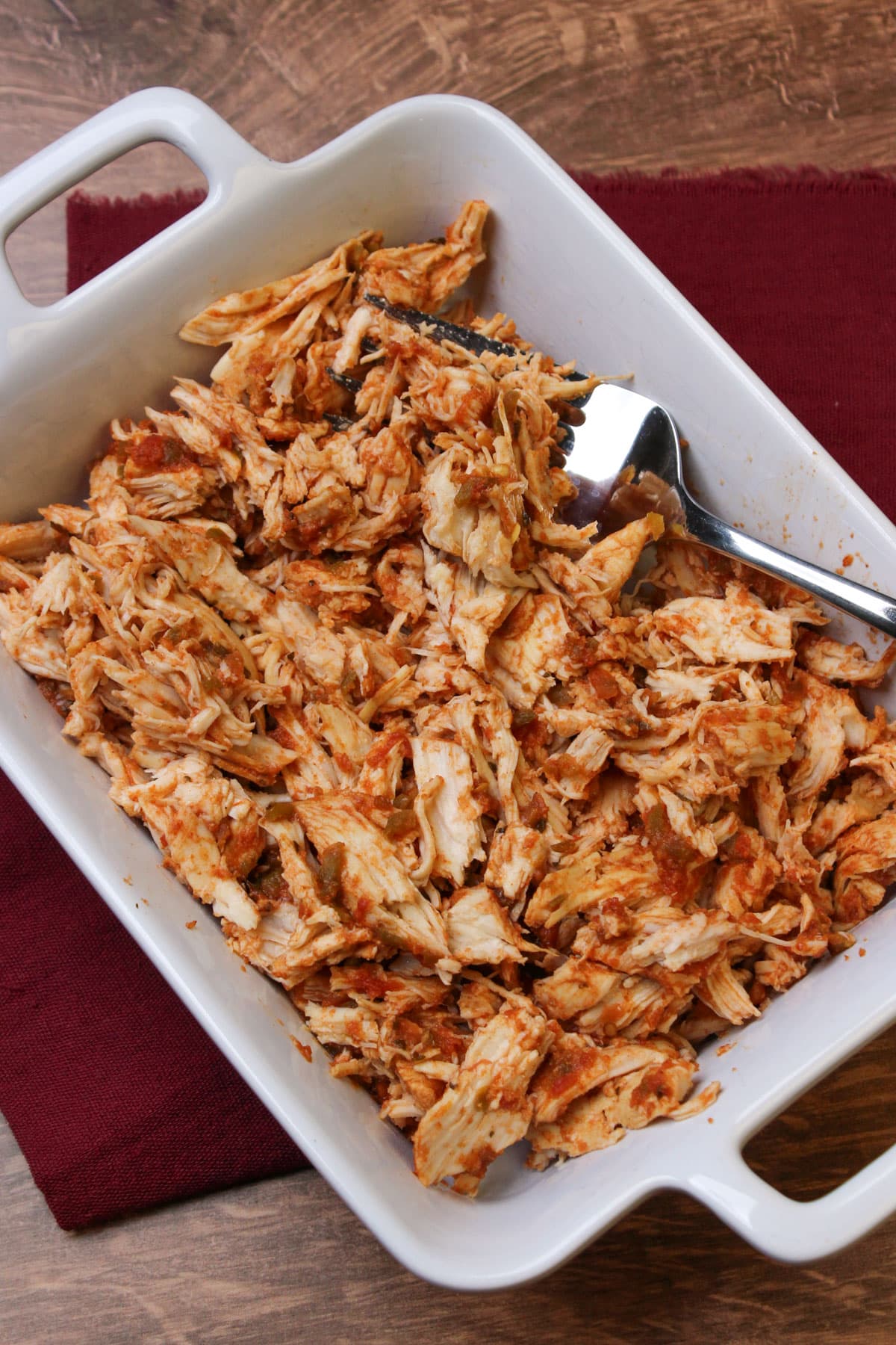 Shredded salsa marinated chicken in a white serving dish with a large fork for serving.