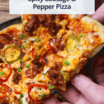 A slice of spicy sausage pizza with fresno and cherry peppers being held over the rest of the pizza.