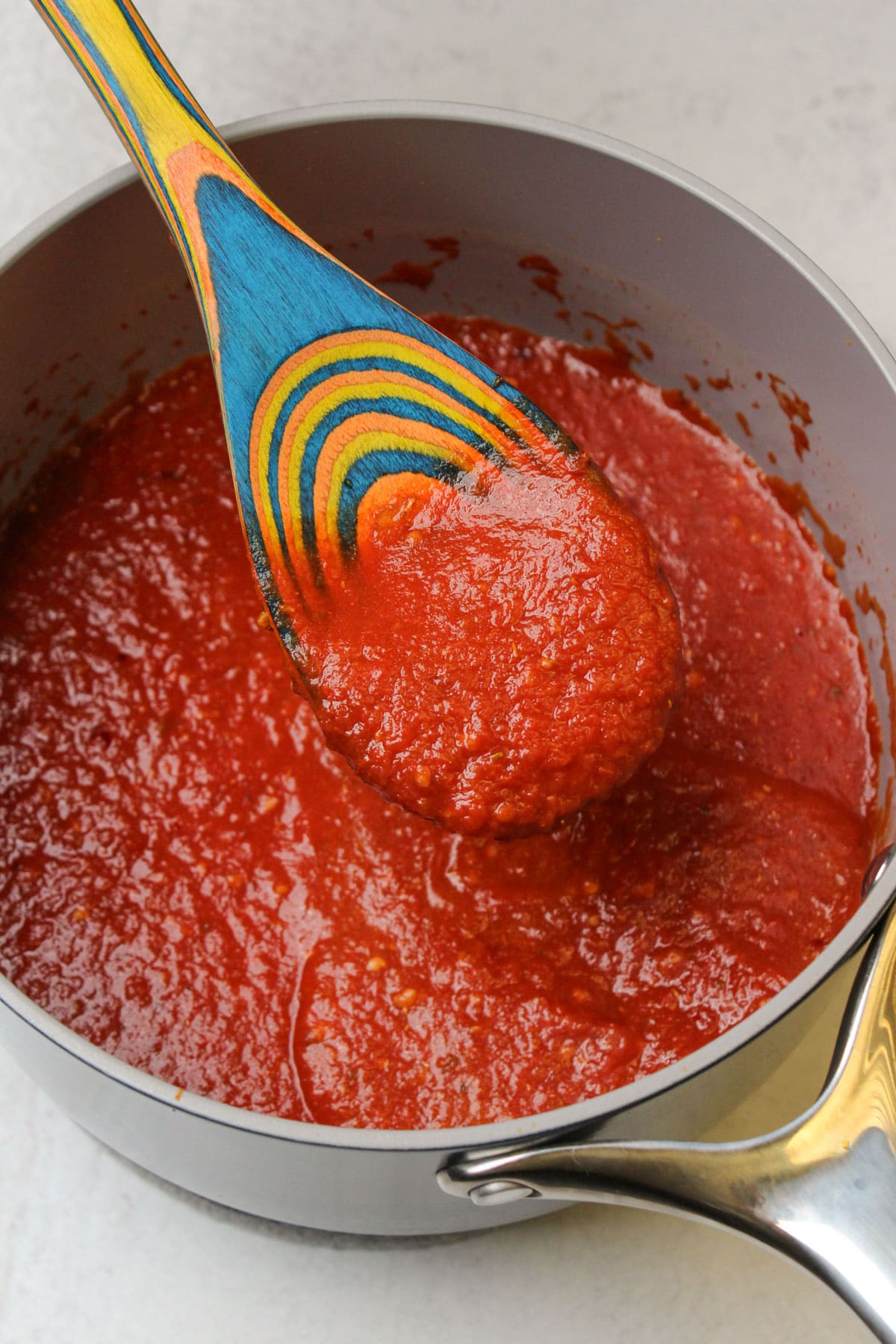 A wooden spoon scooping freshly made spicy Calabrian chili pizza sauce out of a ceramic saucepan.