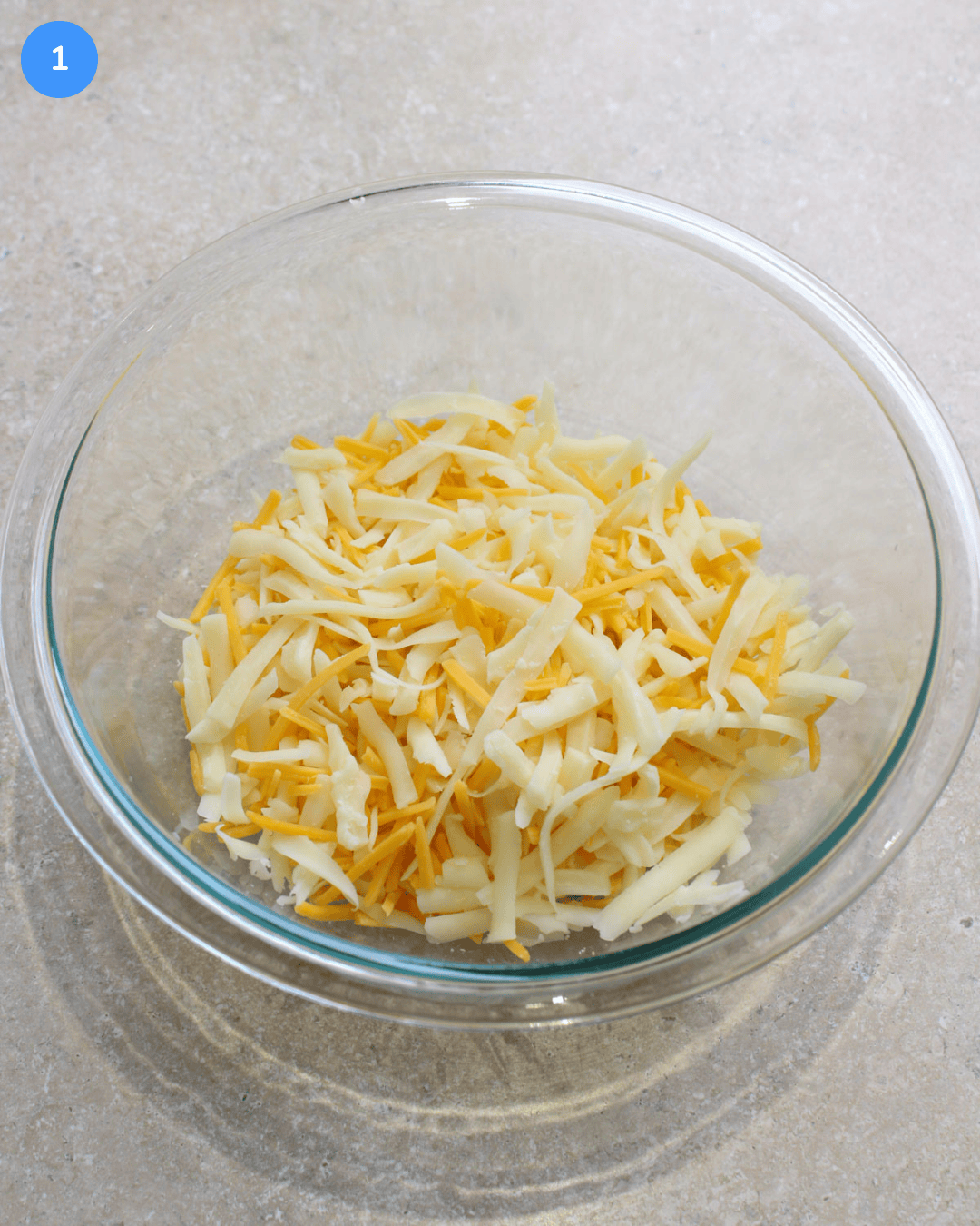 Shredded mozzarella, Monterey jack, and cheddar in a glass mixing bowl.