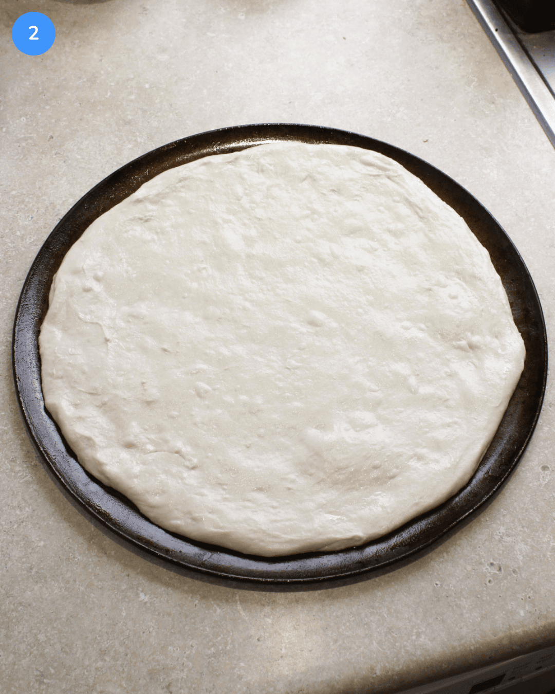 A fresh ball of pizza dough stretched into a large circle on a round pizza pan.