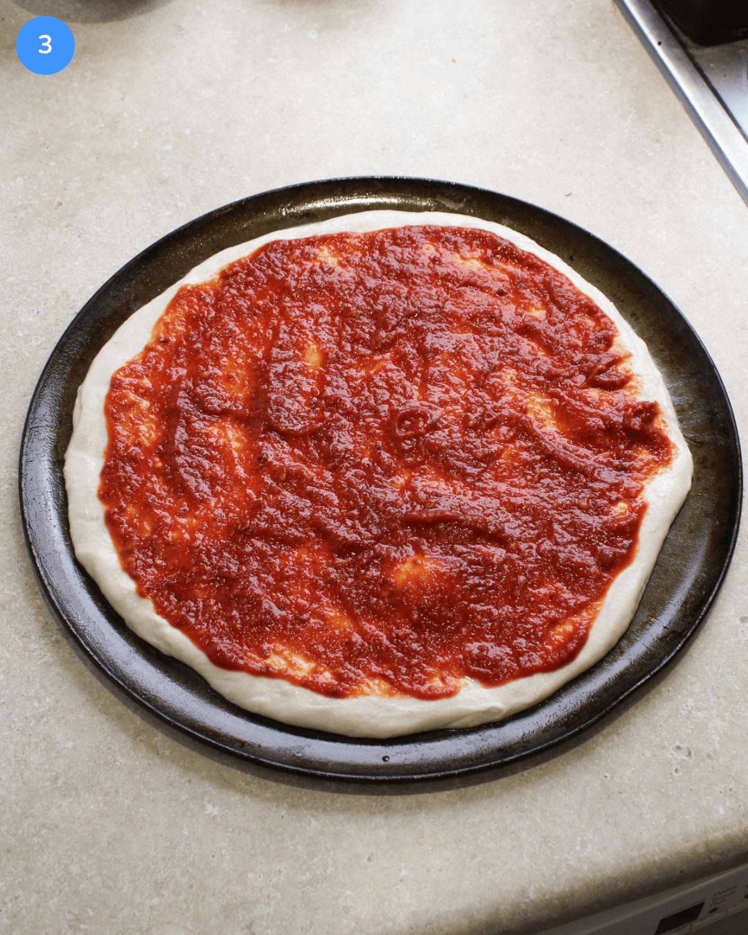 Pizza dough on a round pan topped with a thick layer of spicy red pizza sauce.