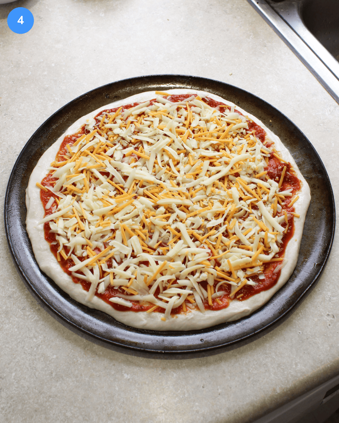 Pizza dough on a round pan topped with spicy red sauce and a blend of freshly shredded cheeses.