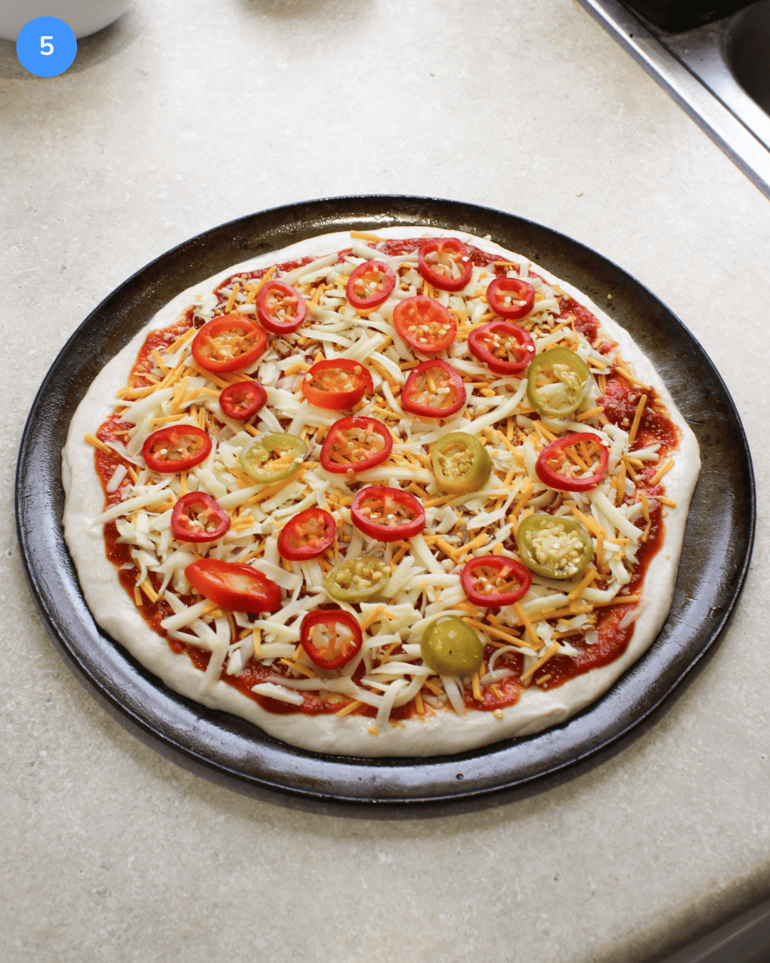 An uncooked pizza topped with spicy red sauce, mixed cheeses, and slices of hot cherry peppers and fresno peppers.