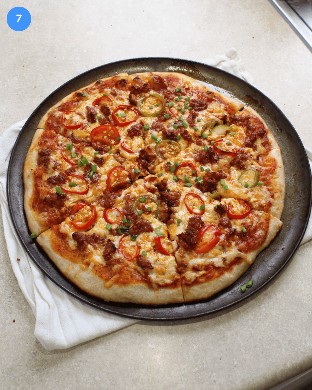A freshly baked spicy sausage and pepper pizza on a round pizza pan.