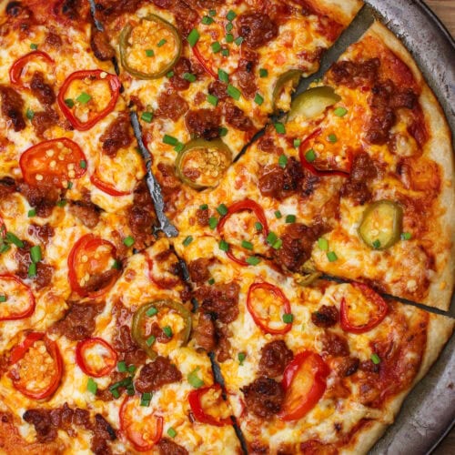 A freshly baked pizza topped with spicy red sauce, cheese, hot cherry pepper slices, fresno pepper slices, and ground Italian sausage.