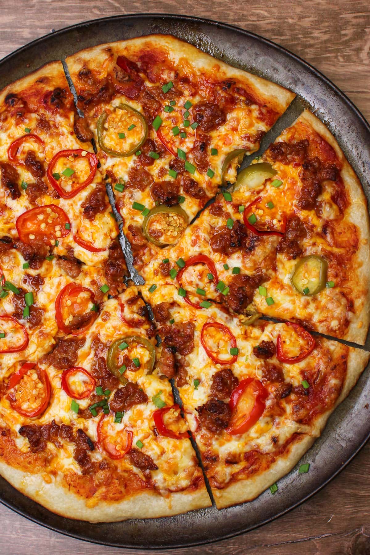 A freshly baked pizza topped with spicy red sauce, cheese, hot cherry pepper slices, fresno pepper slices, and ground Italian sausage.