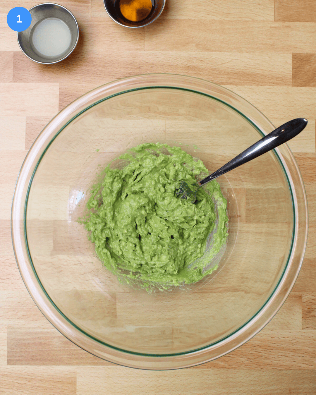 A large glass mixing bowl filled with freshly mashed avocado.