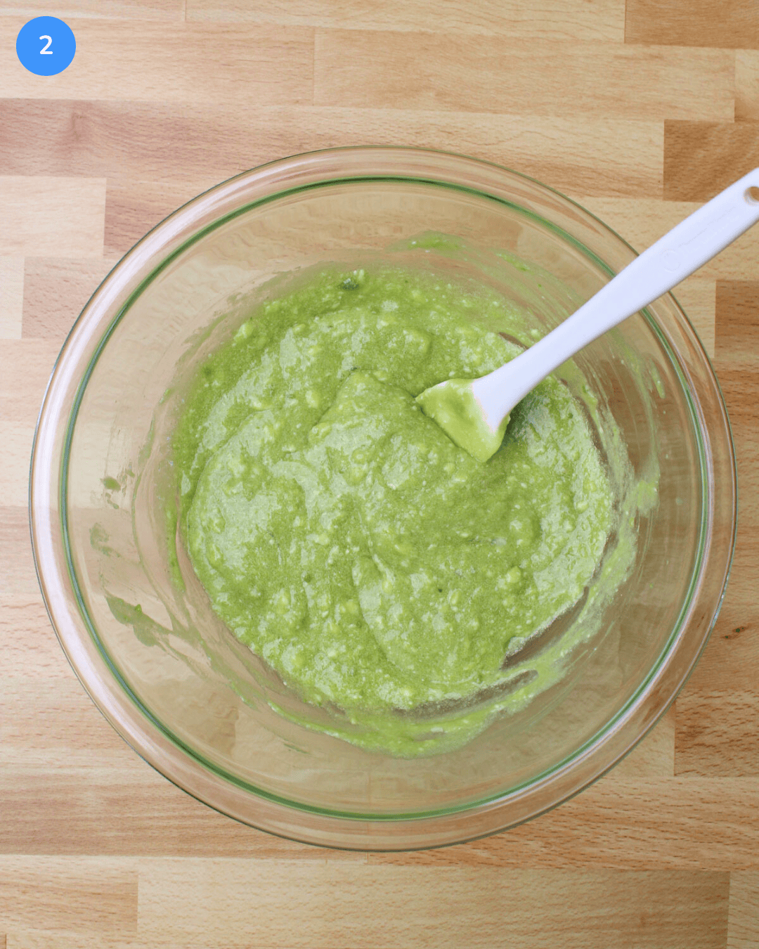 A large glass mixing bowl filled with a mixture of mashed avocado, butter, sugar, egg, vanilla, and lime juice.