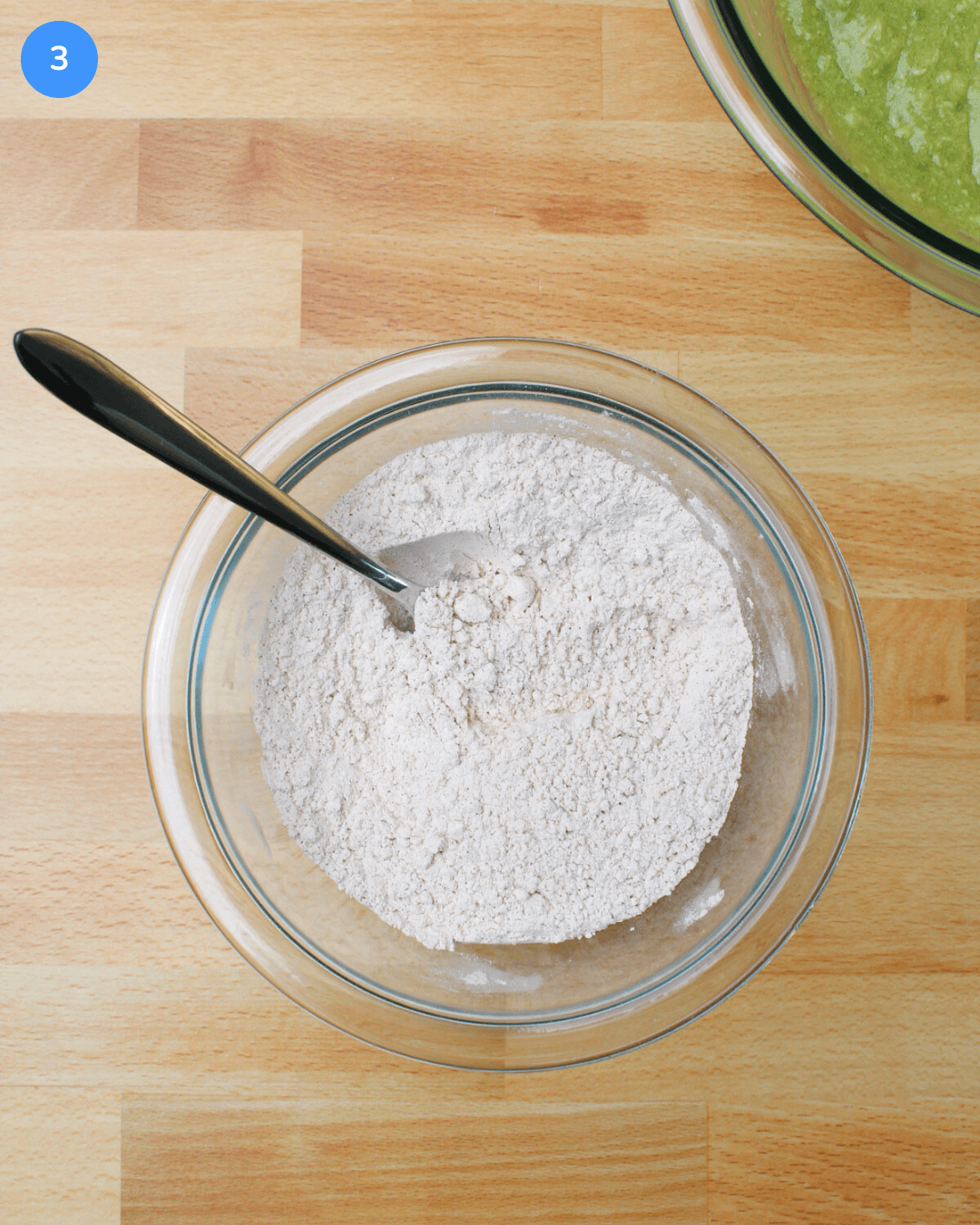 A small glass mixing bowl filled with a mixture of flour, baking soda, baking powder, cinnamon, and salt.