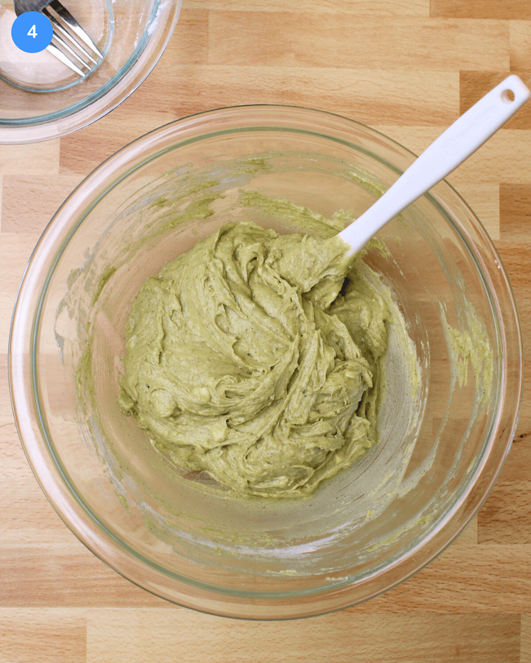 A large glass mixing bowl filled with freshly mixed avocado muffin batter.