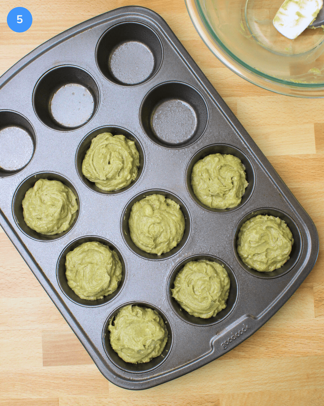 A muffin tin with 8 wells filled with avocado muffin batter.