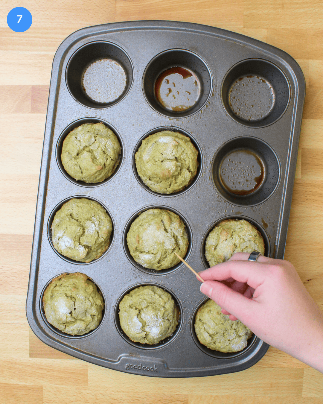A freshly baked tray of avocado muffins being checked for doneness with a toothpick.